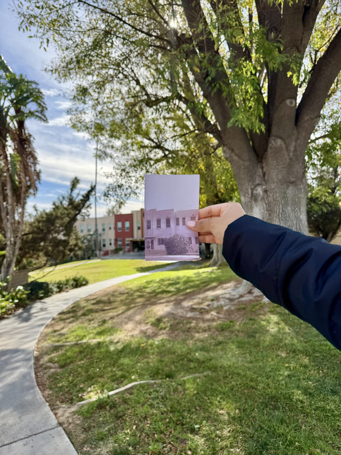A hand holding an archive photograph of the campus in front of the same view today.