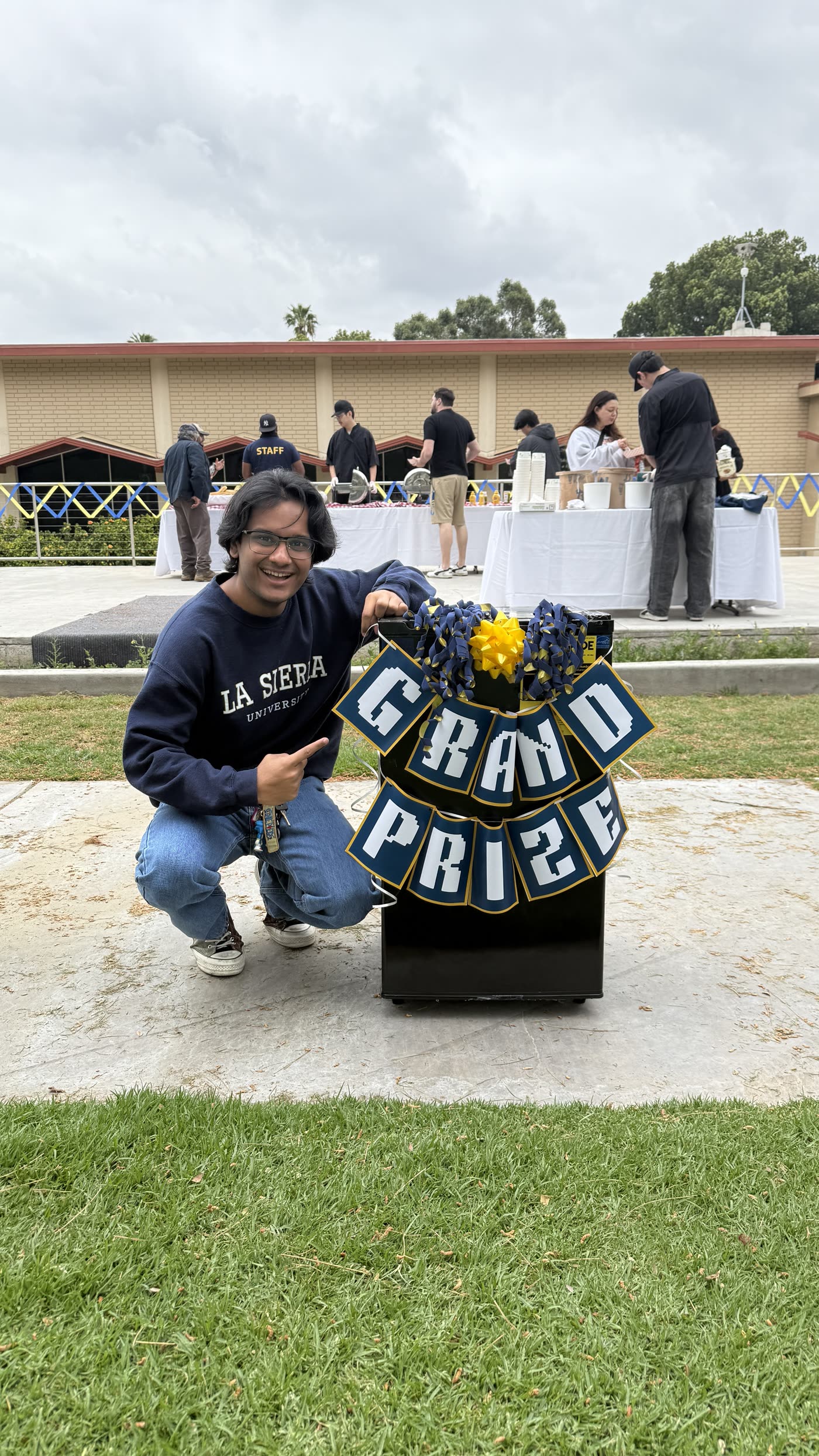 A student kneeling beside a Grand Prize sign at a campus giveaway.