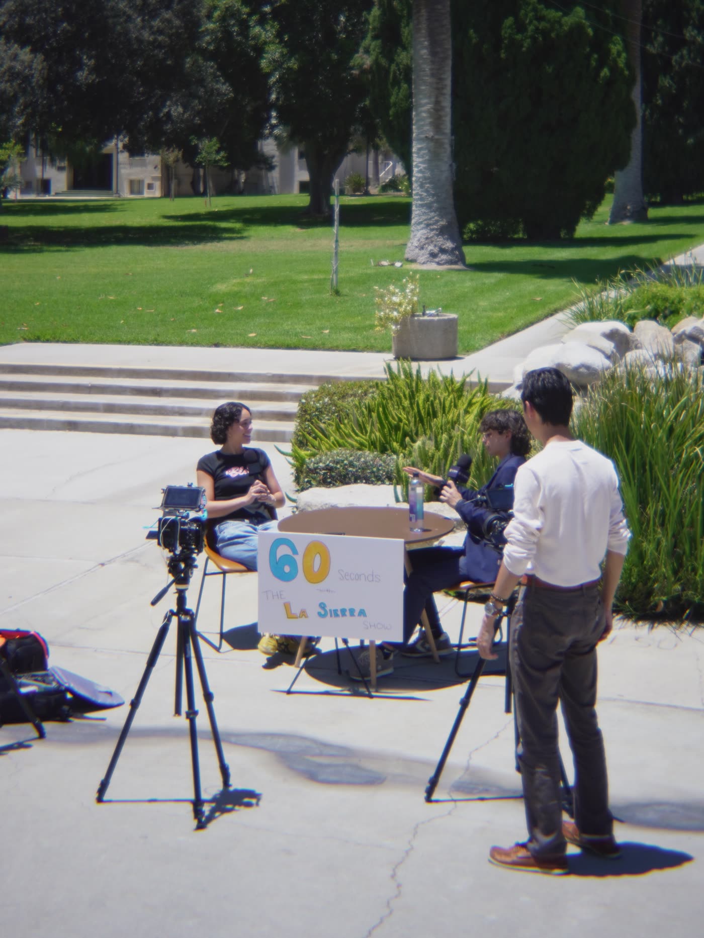 A camera on a tripod filming two people at a table outdoors.